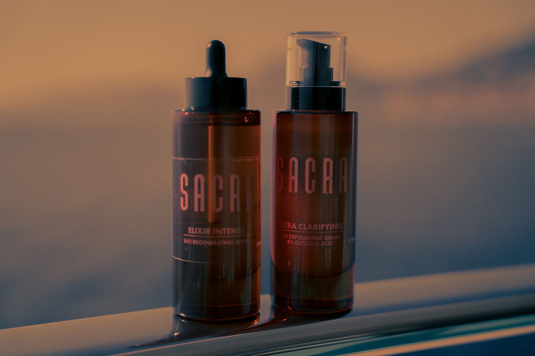 Two SACRA amber bottles on a boat rail at sunset