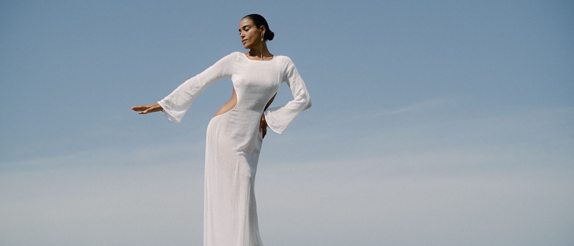 A woman in white on a granite rock, arms open to the sea