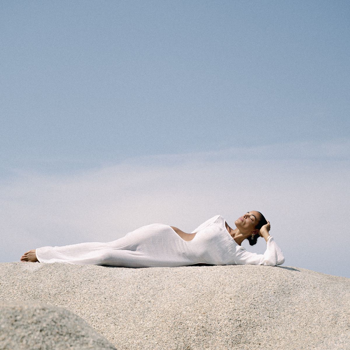 A woman resting on a sunlit granite rock under a clear sky