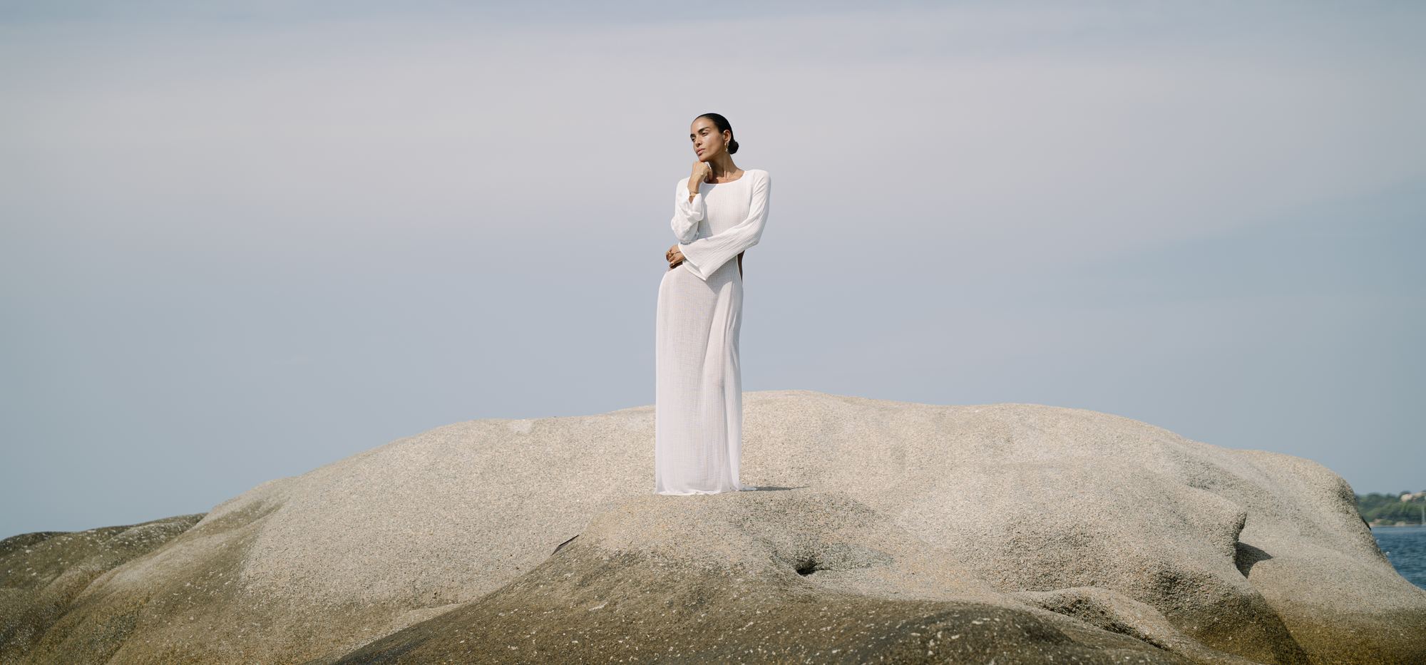 A woman in a white dress standing on a granite rock in the sea